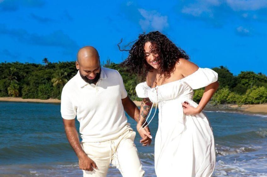 A couple walking on a beach with ocean and greenery in the background. 1