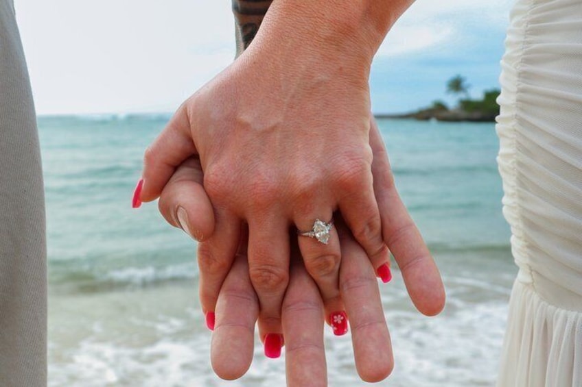 A couple holding hands with a ring on one hand, standing by the ocean. 3