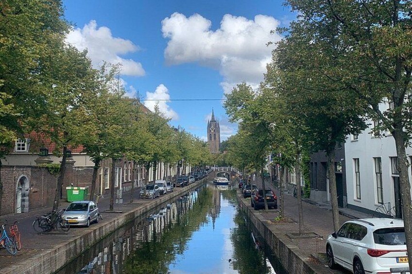 A canal lined with trees and parked cars, with a building and a tower in the background. 3