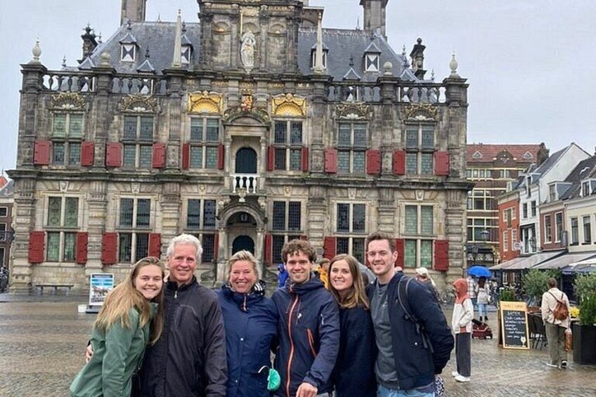 A group of people posing in front of a historic building with red shutters and a clock tower. 1