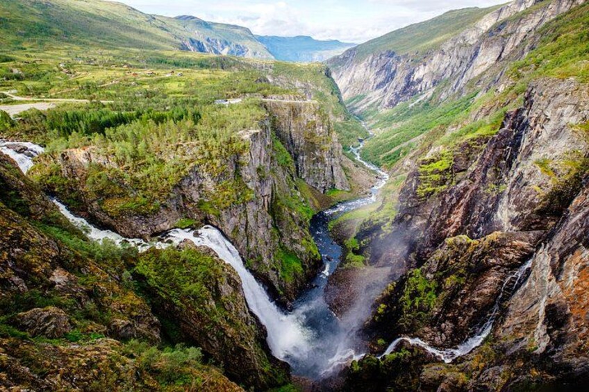 A canyon with a waterfall, river, and surrounding greenery. 2