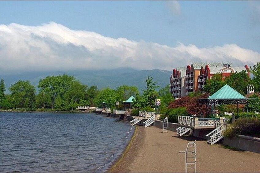 A lakeside walkway with a bridge, buildings, and a gazebo. 4
