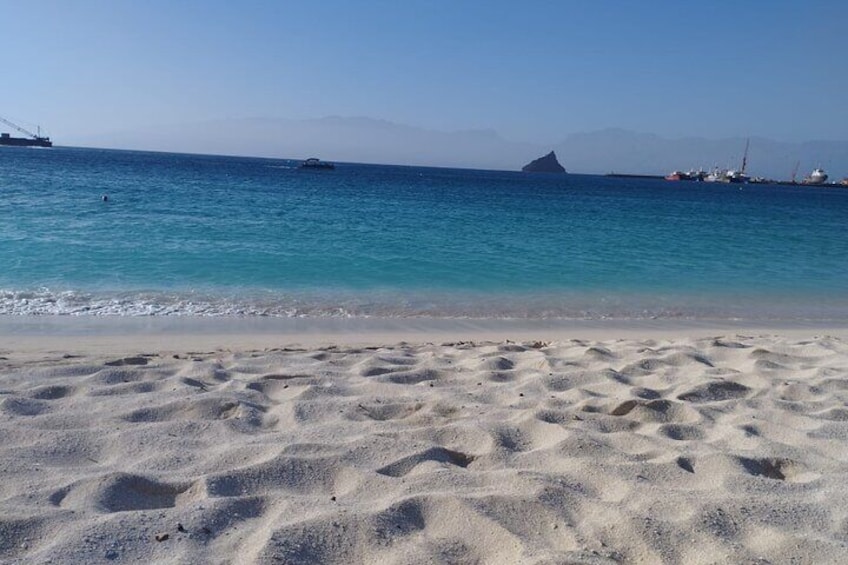 Una playa arenosa con aguas azules cristalinas, barcos y una isla distante. 2