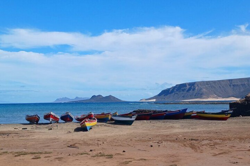 Una playa con varios botes coloridos alineados en la arena, un cielo azul despejado y montañas distantes. 4