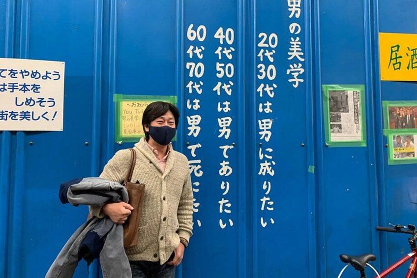 En person som står framför en blå vägg med vertikal japansk text. 2