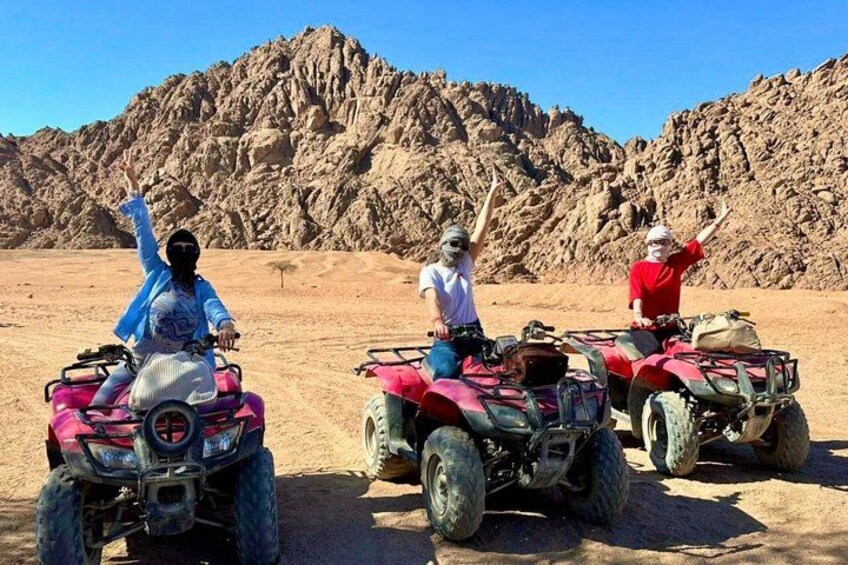 Three people on ATVs in a desert with rocky mountains in the background. 3