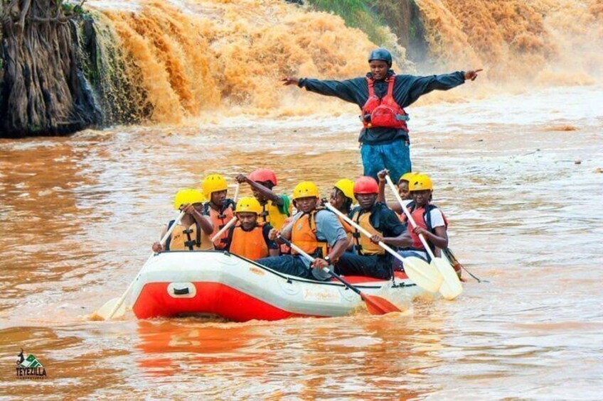 A group of people in a raft navigating a river with a waterfall in the background. 1