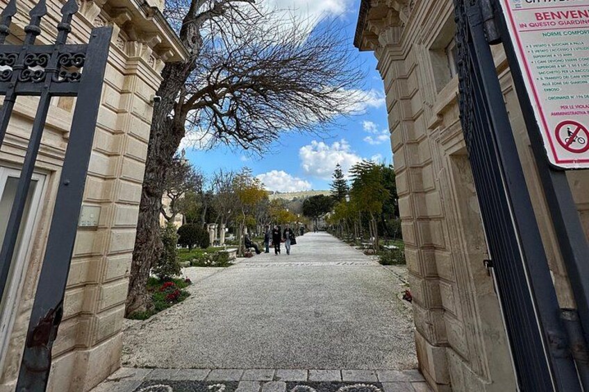 A paved pathway flanked by buildings with a signboard on the right. 5