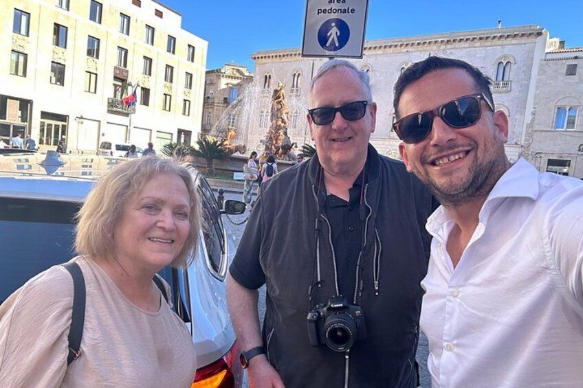Three people taking a selfie with a historic fountain and buildings in the background. 3