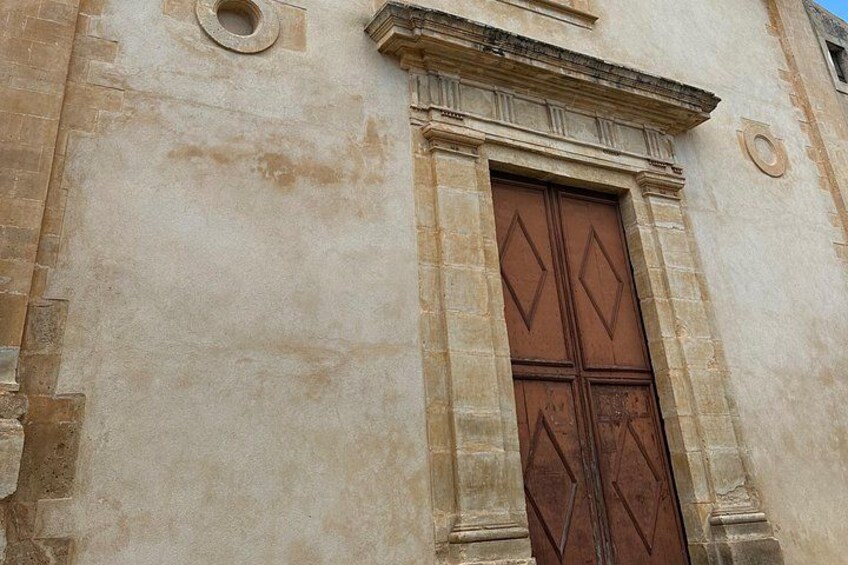 A weathered stone building with a large, ornate wooden door. 4