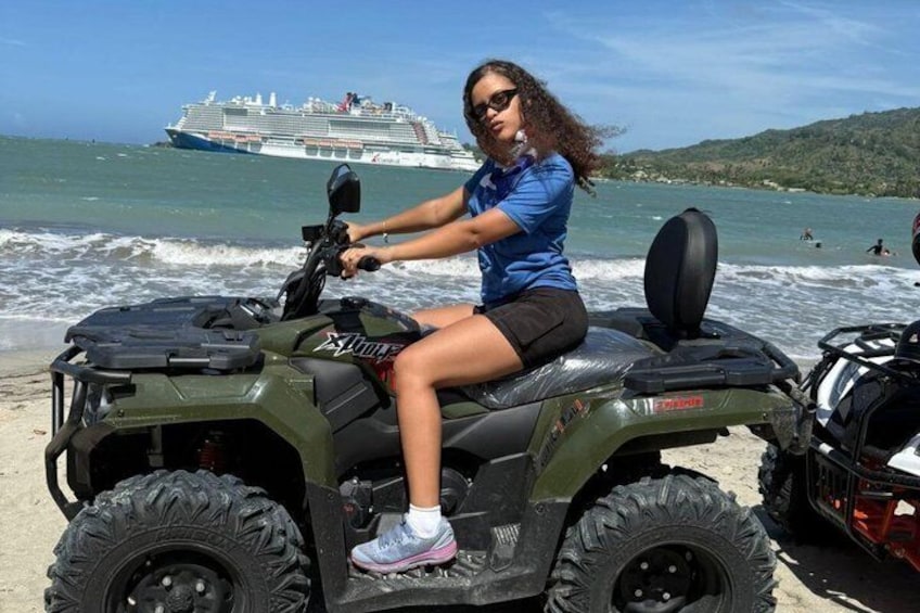 A person riding an ATV on a beach with a cruise ship in the background. 1