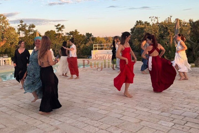 Un grupo de personas bailando al aire libre en un patio con piscina y árboles al fondo. 1