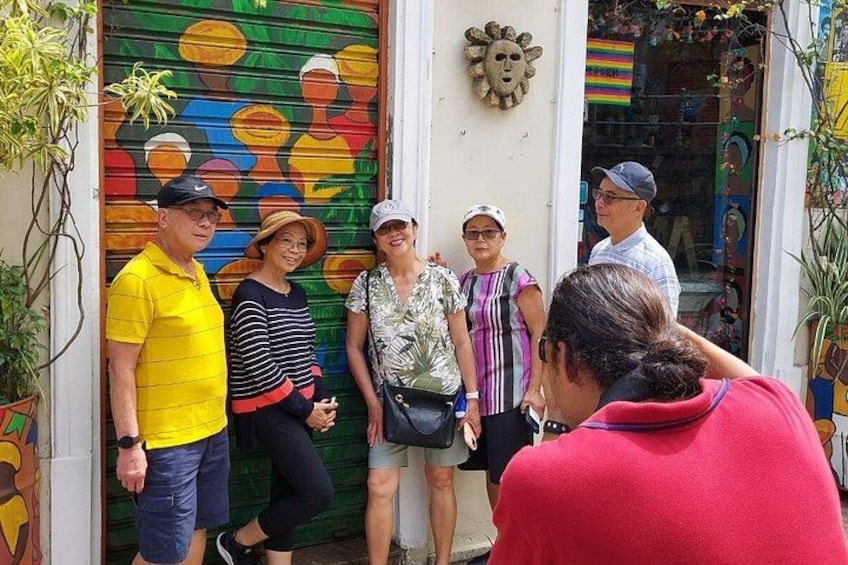 Un gruppo di persone in piedi di fronte a un murale colorato e a un negozio con una persiana verde. 1