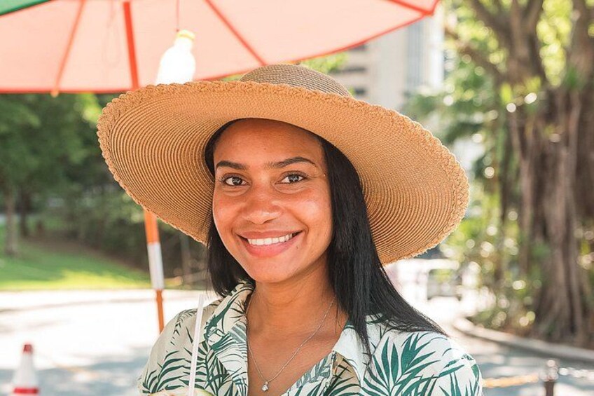 Una persona con un cappello di paglia e una camicia a fantasia tropicale, in piedi sotto un ombrello. 4