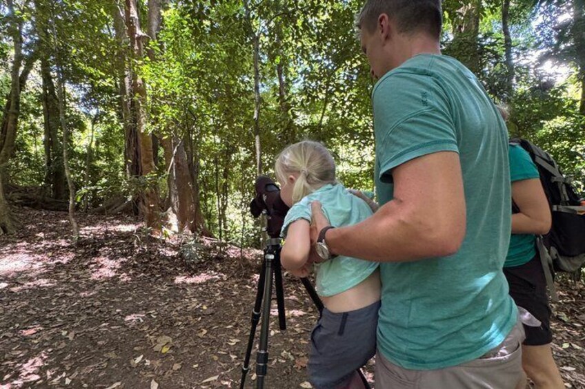 A person holding a child in a forested area with a tripod and camera. 2
