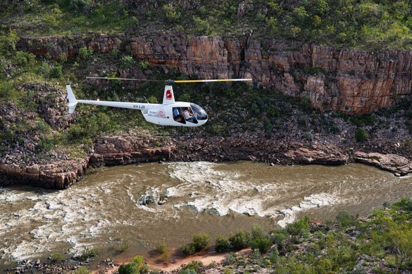 En helikopter flyver over en flod med klippefyldte skråninger i baggrunden. 1
