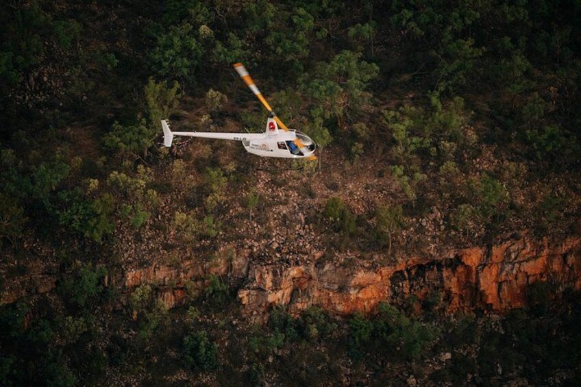 A helicopter flying over a forested area with rocky cliffs. 3