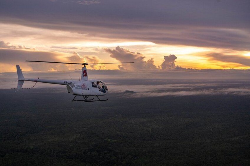 A helicopter flying over a forested landscape during sunset. 1