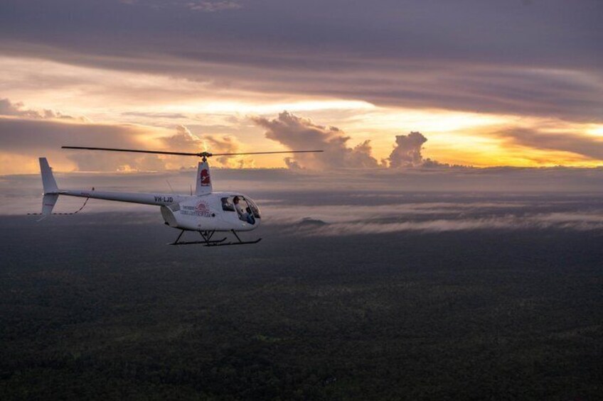 Un helicóptero volando sobre un paisaje boscoso durante la puesta de sol. 1