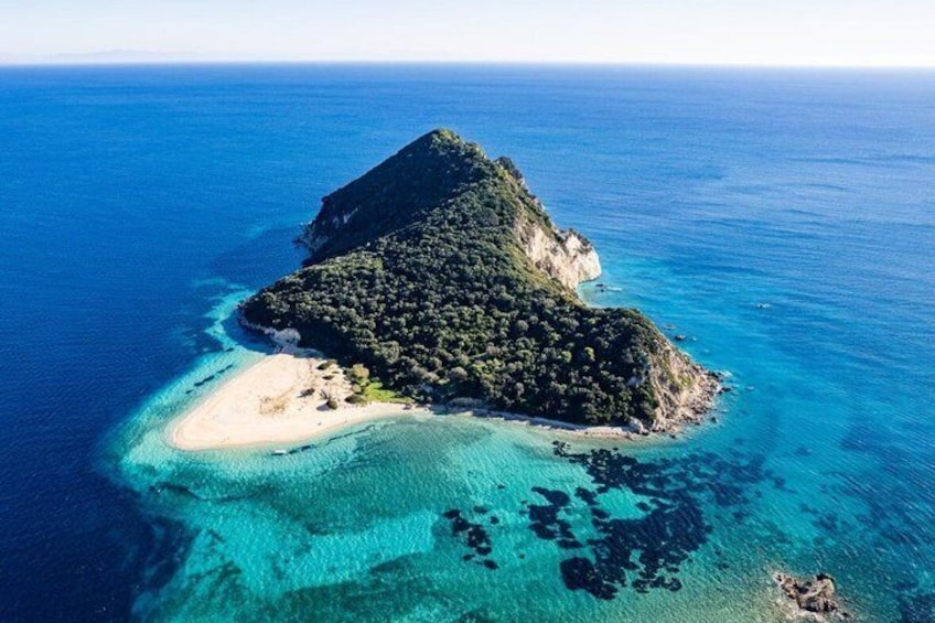 Vista aérea de una pequeña isla con un pico central, rodeada de aguas azules cristalinas y una playa de arena. 4