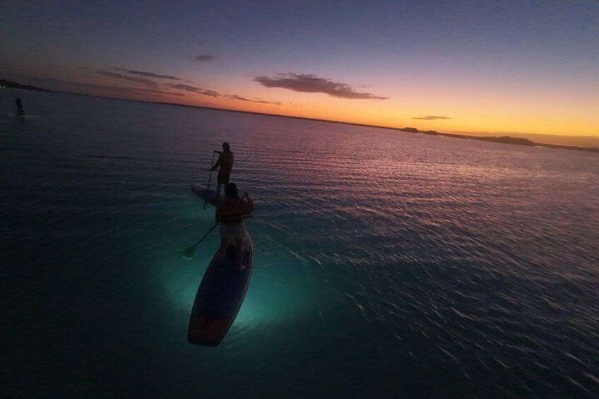 Eine Person steht bei Sonnenuntergang auf einem Paddleboard auf ruhigem Wasser. 3
