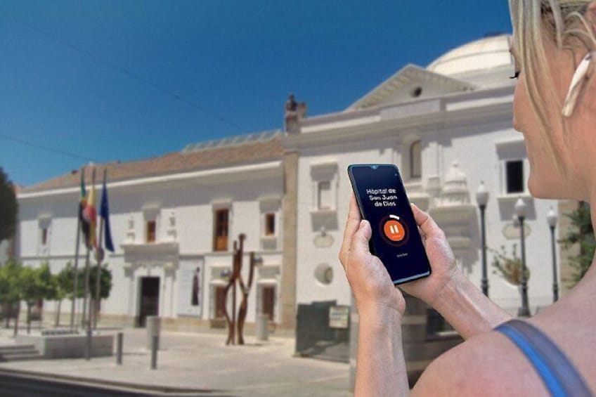 A person using a smartphone with a hospital app interface, standing in front of a white building with columns and a dome. 5