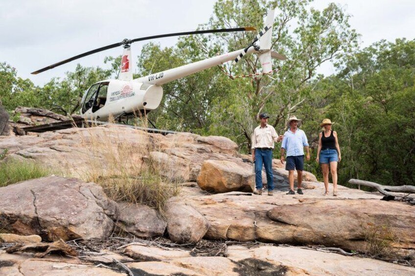 A helicopter on a rocky outcrop with three people standing nearby. 3