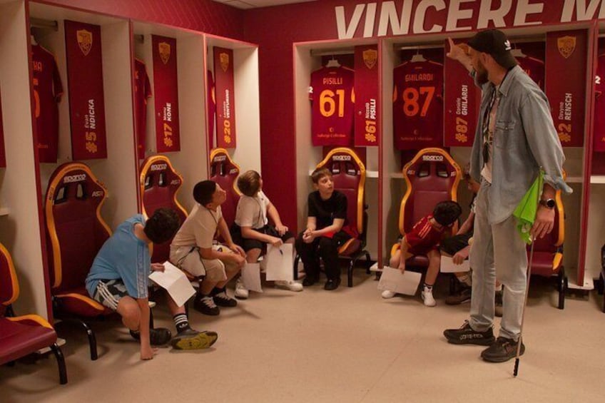 A sports locker room with numbered benches, a person standing, and children sitting. 5