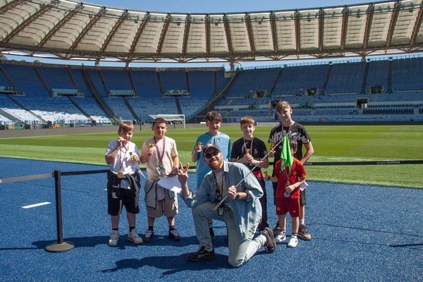 A group of people posing in a stadium with blue seats and a green field. 1