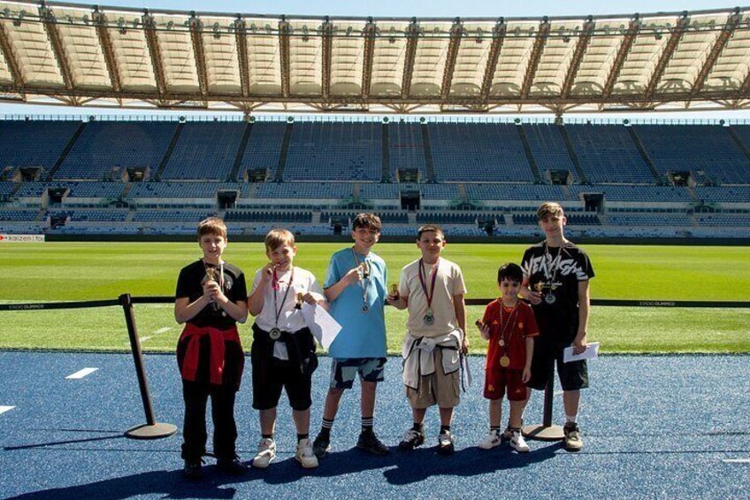 A group of people standing on a sports field with a stadium in the background. 3