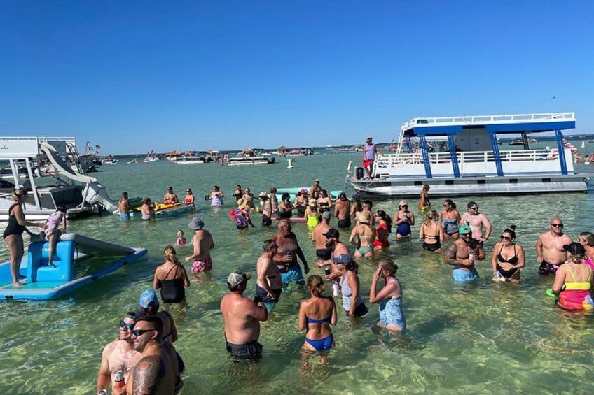 Ein überfüllter Strand mit Menschen im Wasser und Booten im Hintergrund. 4