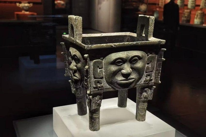 A historical artifact with a carved face, displayed on a pedestal in a museum setting. 1