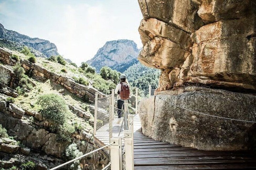 A person walking on a wooden bridge over a rocky canyon with mountains in the background. 1