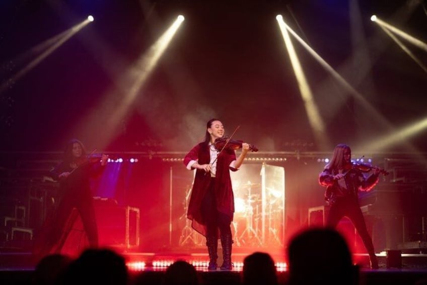 A violinist performing on stage with stage lights and a drum set in the background. 2