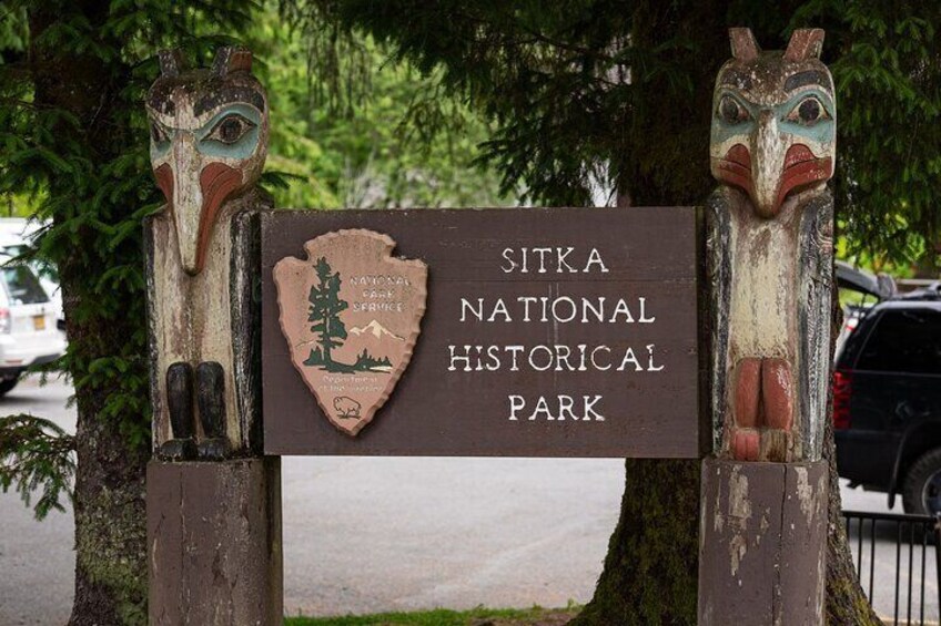 A sign for Sitka National Historical Park with two totem poles. 1