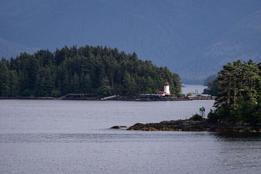 A lighthouse on a rocky island surrounded by calm water and dense forest. 5