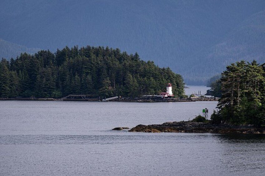 A lighthouse on a rocky island surrounded by calm water and dense forest. 5