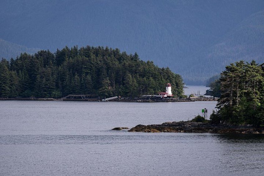 A lighthouse on a rocky outcrop surrounded by dense forest and a calm body of water. 3