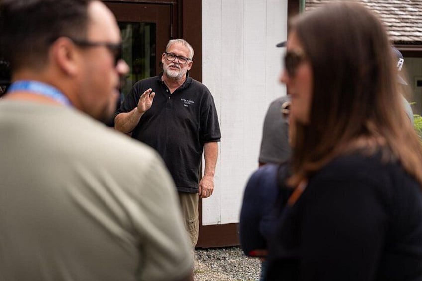 A man in a black polo shirt speaking to a group of people. 4