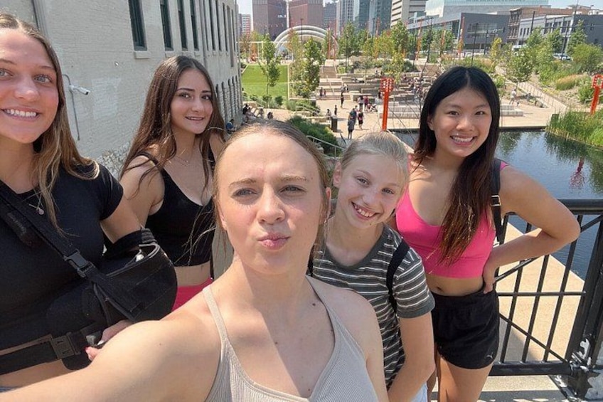 Een groep mensen maakt een selfie op een brug, met een stadsgezicht op de achtergrond. 2