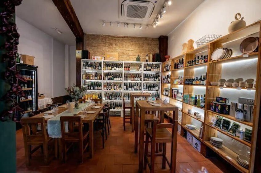 A cozy restaurant with wooden tables and chairs, shelves of wine bottles, and various kitchenware. 2