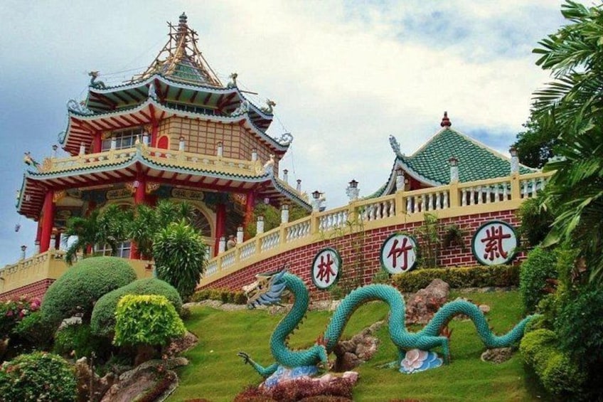 Una pagoda china tradicional con arquitectura elaborada, un jardín cuidado con una escultura de dragón y un cielo despejado. 1