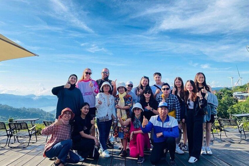 Un groupe de personnes posant sur une terrasse en bois, avec une vue panoramique sur les montagnes en arrière-plan. 3