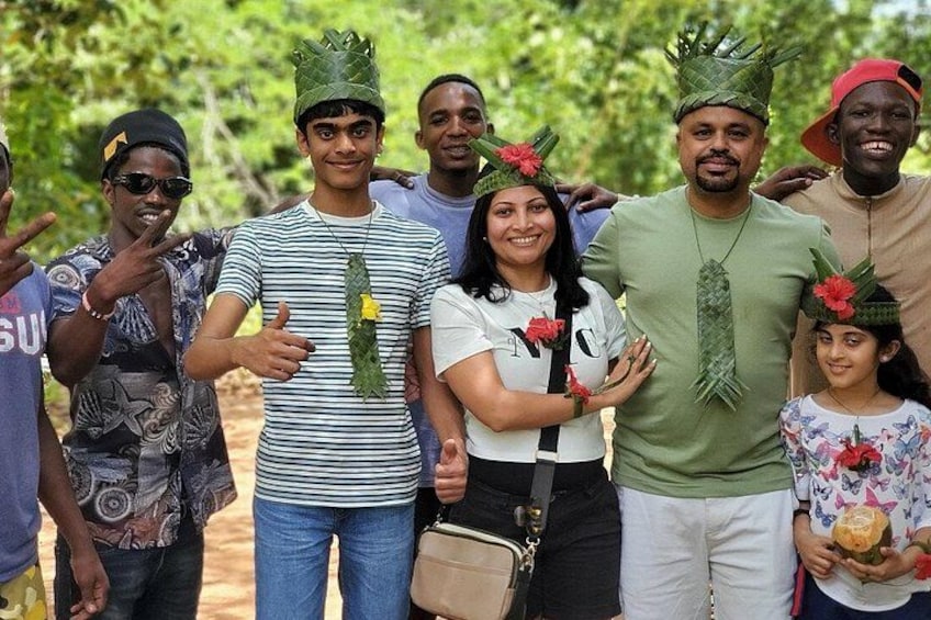Un grupo de personas al aire libre, algunas con sombreros verdes adornados con hojas, de pie en un entorno natural con árboles al fondo. 3