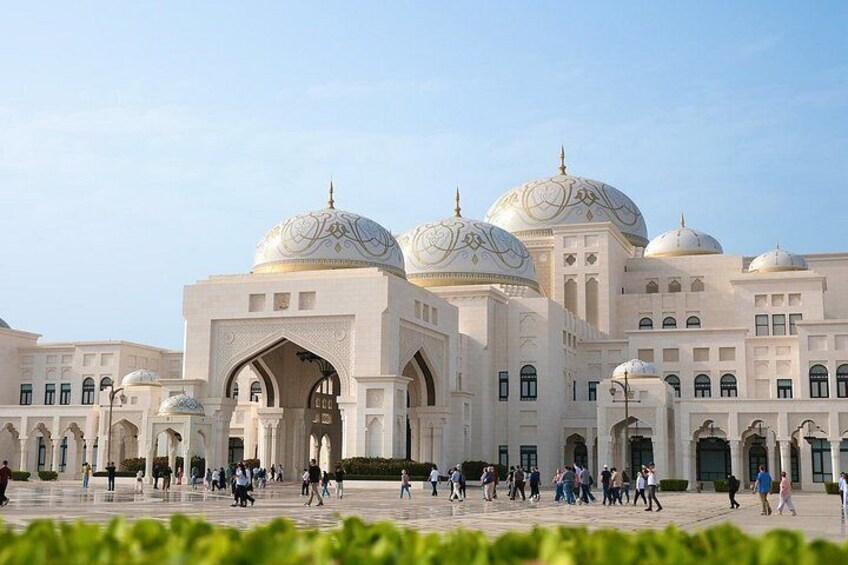 A large, white building with multiple domes and arches, surrounded by a spacious courtyard with people walking. 3
