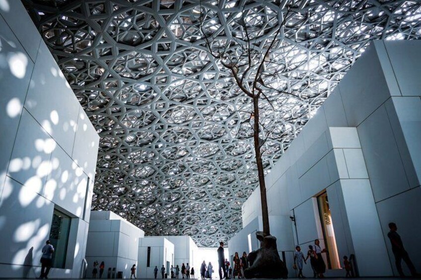 A modern architectural structure with a complex geometric ceiling design and a central tree. 1