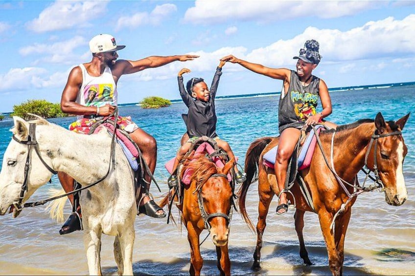 Drei Personen reiten Pferde am Strand, im Hintergrund das Meer. 1