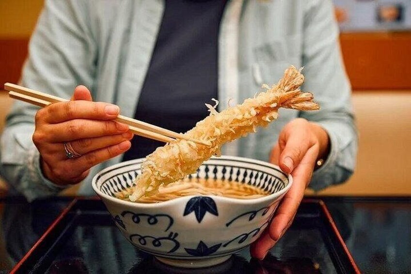 A person holding a bowl of ramen with chopsticks. 3