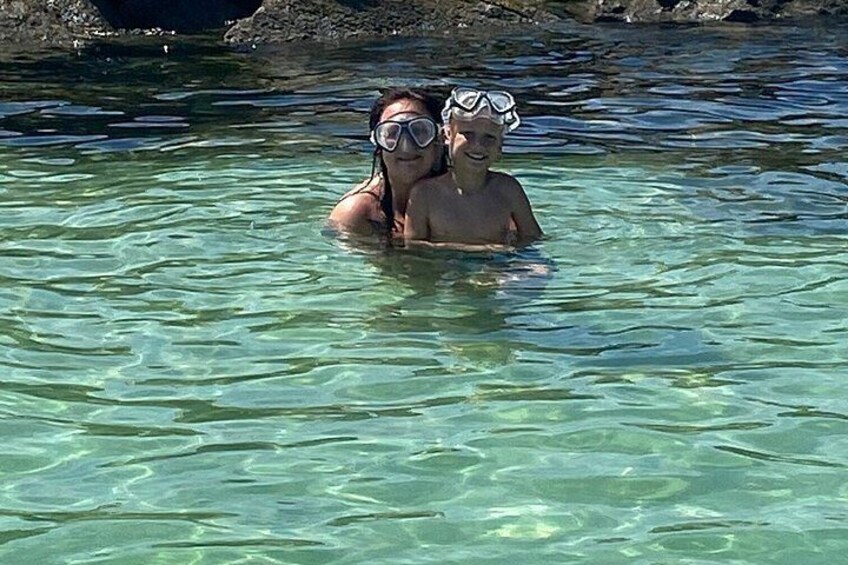 Two people snorkeling in clear water with rocks in the background. 2