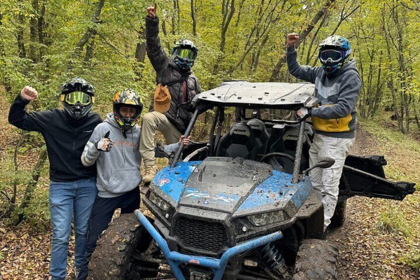 A group of people with a blue off-road vehicle in a forest. 2